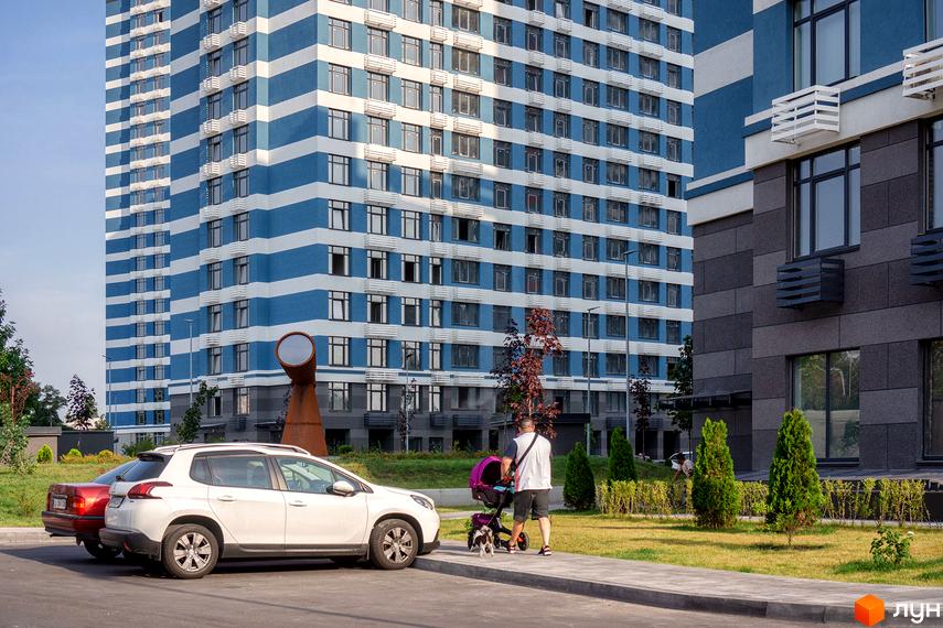 Новобудова ЖК Галактика з синьо-білим фасадом та кондиціонерами. Прибудинкова територія з доглянутим газоном, деревами та припаркованими автомобілями.