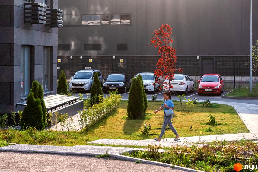 Зовнішній вигляд новобудови ЖК Галактика з паркуванням та зеленими насадженнями. На зображенні видно сучасну архітектуру та доглянуту прибудинкову територію.