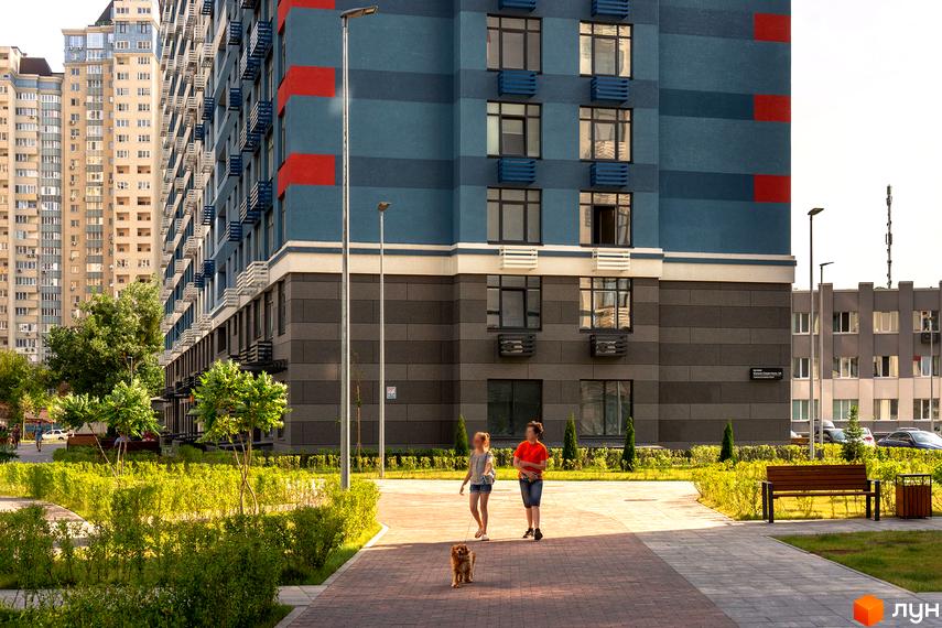 Житловий комплекс Галактика: фасади будівель з синіми та червоними елементами, прибудинкова територія з зеленими насадженнями, доріжками та лавками.