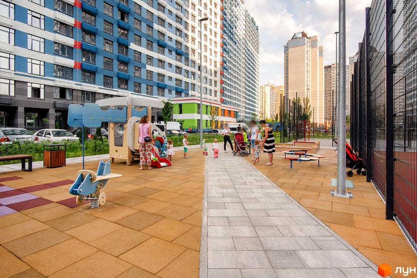 Комплекс Галактика: висотні будинки з блакитними та білими фасадами. Дитячий майданчик з гіркою та гойдалками, зона відпочинку з лавками та огорожею.