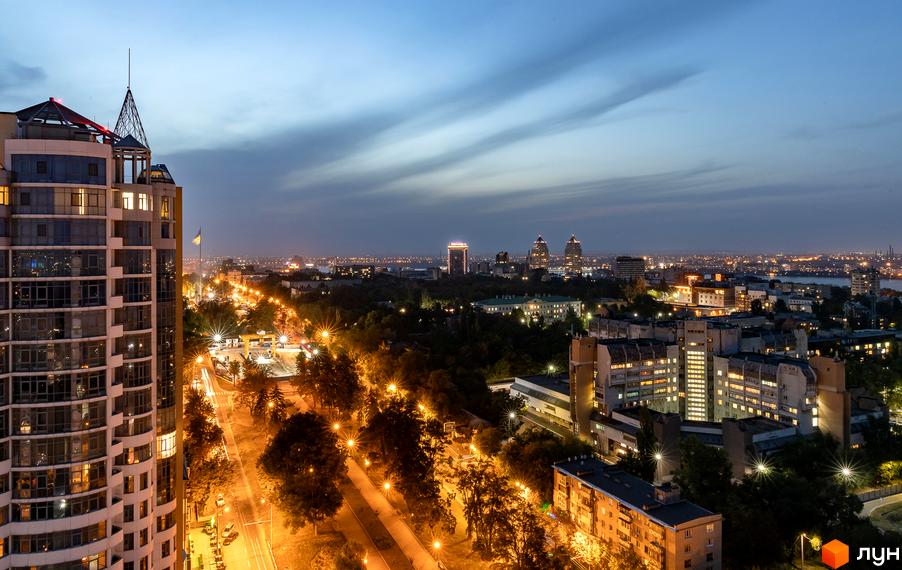 Житловий комплекс Славія на фоні вечірнього міста. Околиці з освітленими вулицями та зеленими насадженнями.