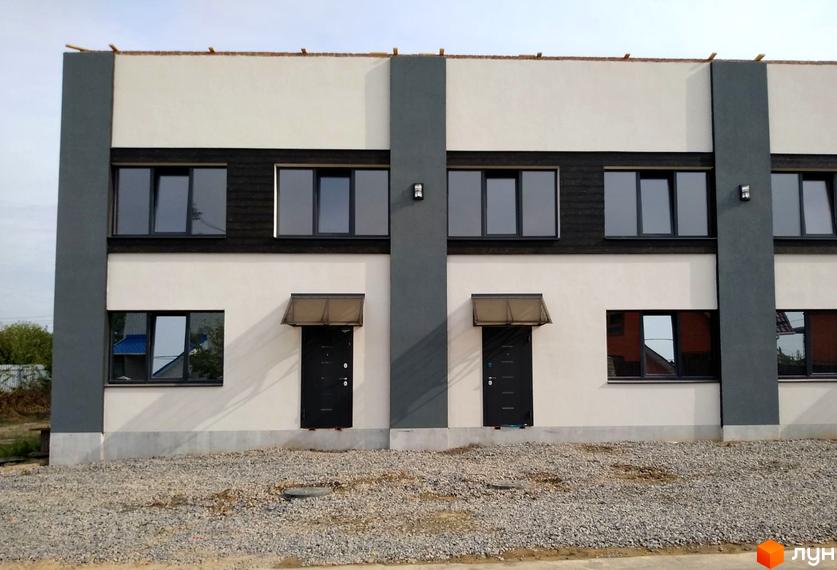 Зовнішній вигляд новобудови на вул. Якова Гальчевського, 102-114, з сірими та білими фасадами, темними вікнами та дверима. Територія перед будинком засипана гравієм.