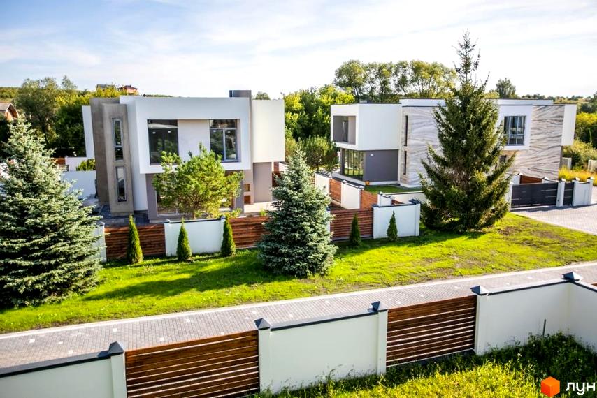 Котеджне містечко КМ Riviera Gold з двома сучасними будинками та доглянутою зеленою територією. Навколо будинків розташовані дерева та огороджена ділянка.