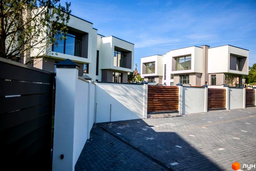 Котеджне містечко Riviera Gold - фасади будинків з великими вікнами та прибудинкова територія з бруківкою та дерев'яними парканами.