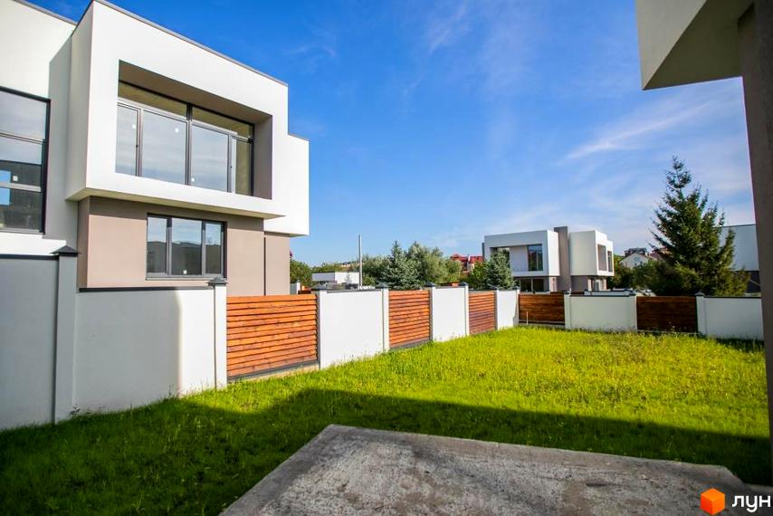 Котеджне містечко Riviera Gold: двоповерхові будинки з великими вікнами та дерев'яними парканами. Зелена галявина перед будинками.