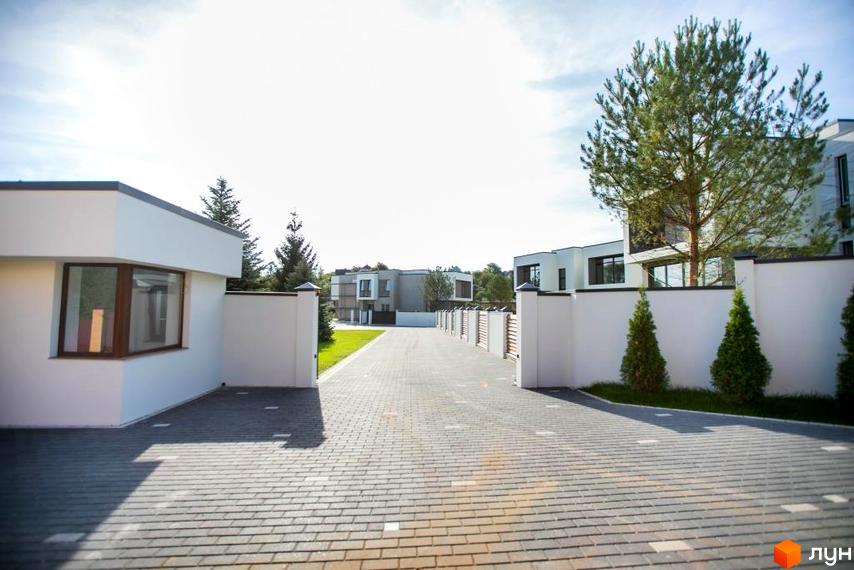 Котеджне містечко КМ Riviera Gold: фасади будинків з великими вікнами, огороджена територія з бруківкою та зеленими насадженнями.