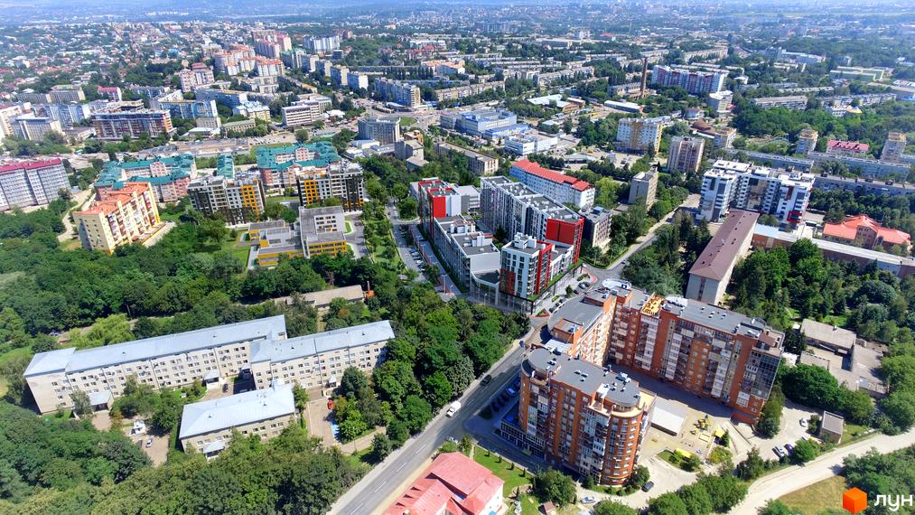 Вид на багатоповерхові будинки ЖК Престижний 2 з червоними та білими фасадами. Навколо будівель зелені насадження та дорога.