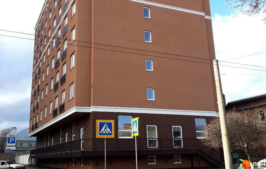 Зовнішній вигляд багатоповерхового будинку ЖК Слов'янський з коричневим фасадом та білою обробкою. Навколо будинку розташовані пішохідні переходи та дерева.