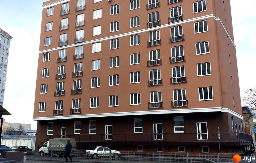 Фасад новобудови ЖК Слов'янський з численними вікнами та балконами. Біля будинку розташовані автомобілі та пішохідна зона.