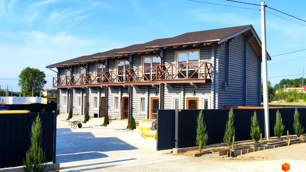 Таунхауси LEVEL – двоповерхові будинки з дерев'яними балконами та парканом навколо території. На прибудинковій території розташовані зелені насадження та будівельні матеріали.