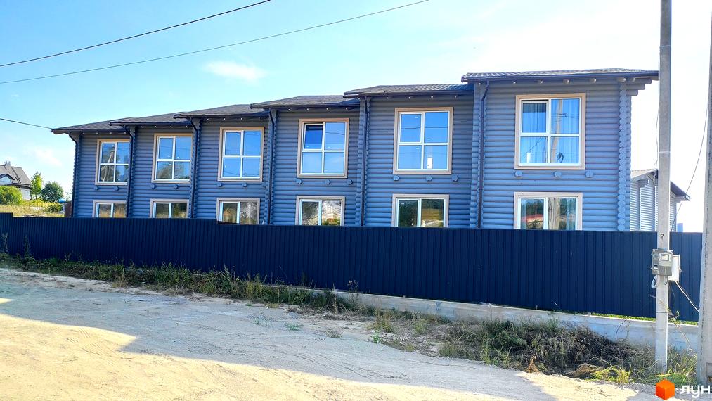 Таунхауси LEVEL – двоповерхові будинки з сірими стінами з брусу та білими вікнами, огороджені темним парканом. Навколо будівель – зелена трава та піщана дорога.