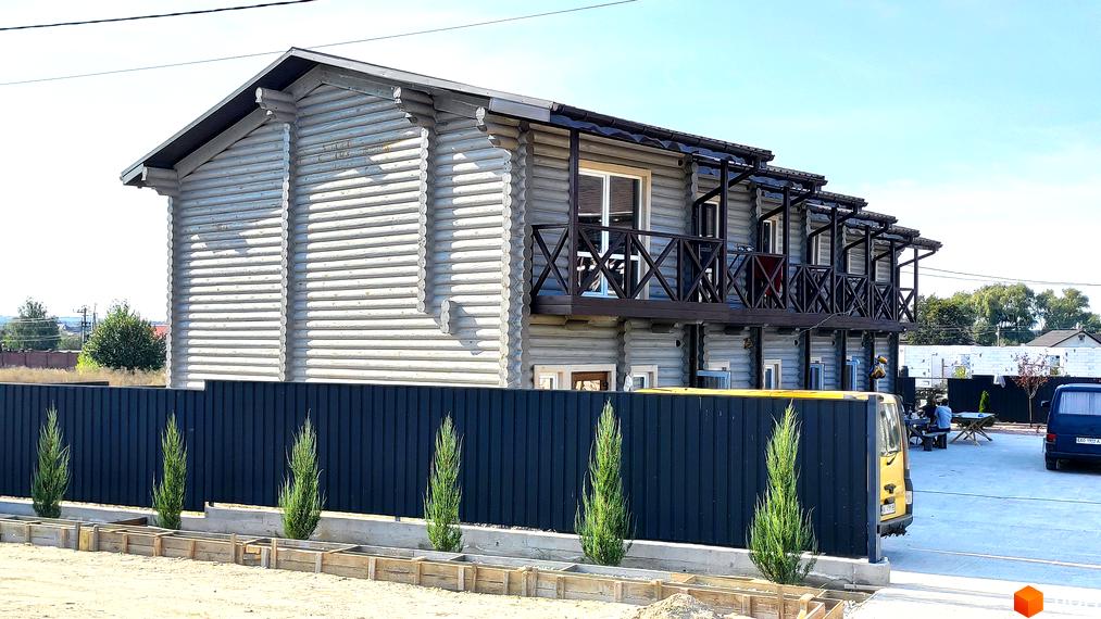 Будинок з брусу з балконами та парканом. На території новобудови LEVEL розташовані автомобілі та місця для відпочинку.