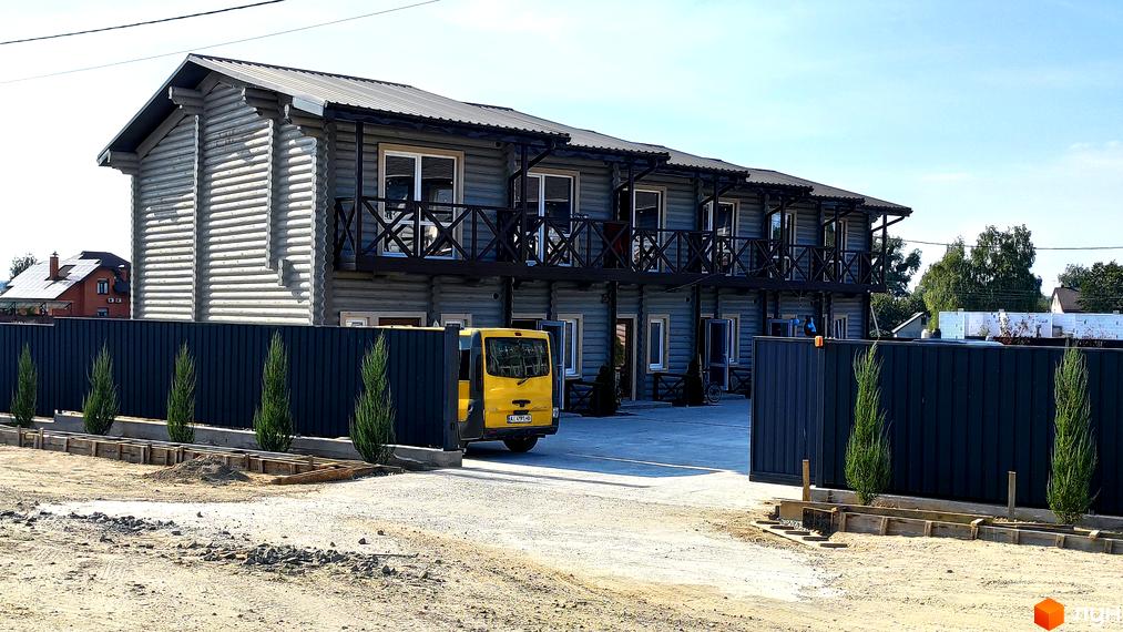 Таунхауси LEVEL – двоповерхові будинки з дерев'яним фасадом та балконами, перед якими розташована парковка та зелені насадження.