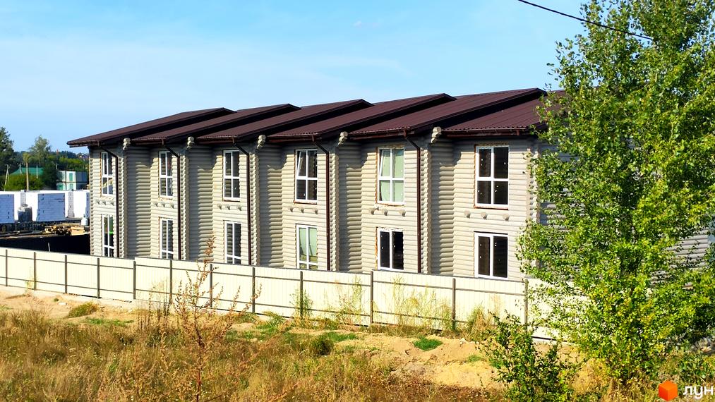 Таунхауси LEVEL – двоповерхові будинки з дерев'яних колод та коричневим дахом, огороджені парканом. Навколо зелені дерева та невисока рослинність.