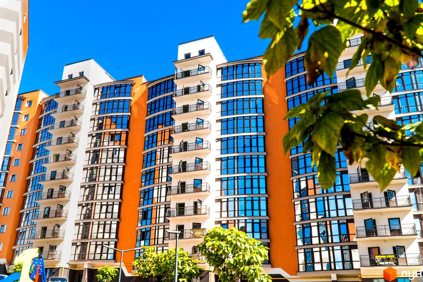 Зовнішній вигляд багатоповерхового будинку з великими вікнами. Житловий комплекс Містечко Соборне з балконами та помаранчевими вставками.