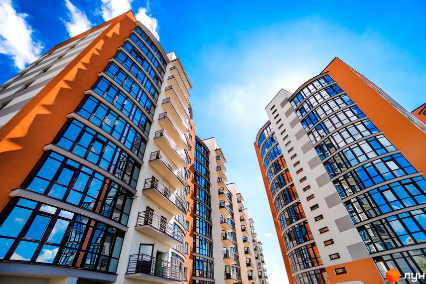 Фото фасаду багатоповерхового будинку Житлового комплексу Містечко Соборне. Вигляд новобудови з великими вікнами та балконами на тлі блакитного неба.