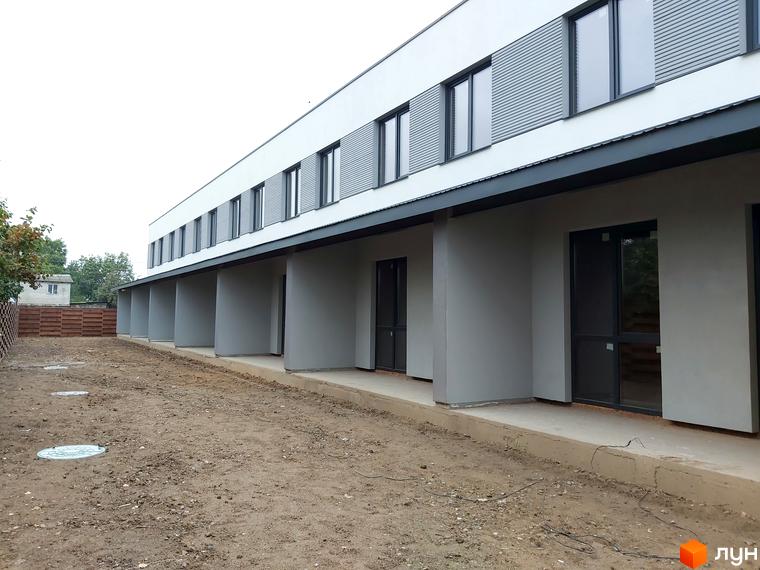 Зовнішній вигляд новобудови на вул. Сергія Колоса, 169 з сірими фасадами та великими вікнами. Прибудинкова територія з ґрунтом та люками.