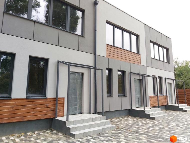 Зовнішній вигляд новобудови на вул. Сергія Колоса, 169, з сірими фасадами, дерев'яними вставками та вимощеною прибудинковою територією. Будинок має кілька входів зі сходами та навісами.