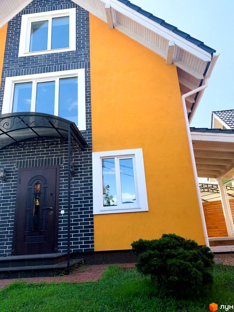 Фасад будинку Котеджного містечка Osocor Scandi House з темно-сірою цегляною кладкою та яскраво-жовтою штукатуркою, білі вікна, зелений газон.