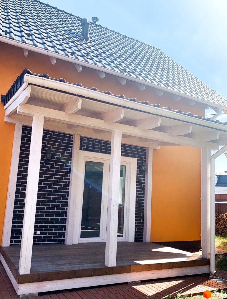Котеджне містечко Osocor Scandi House: будинок з помаранчевим фасадом, темною цегляною стіною та білою дерев'яною верандою. Дах покритий сірою черепицею, перед входом дерев'яна тераса.