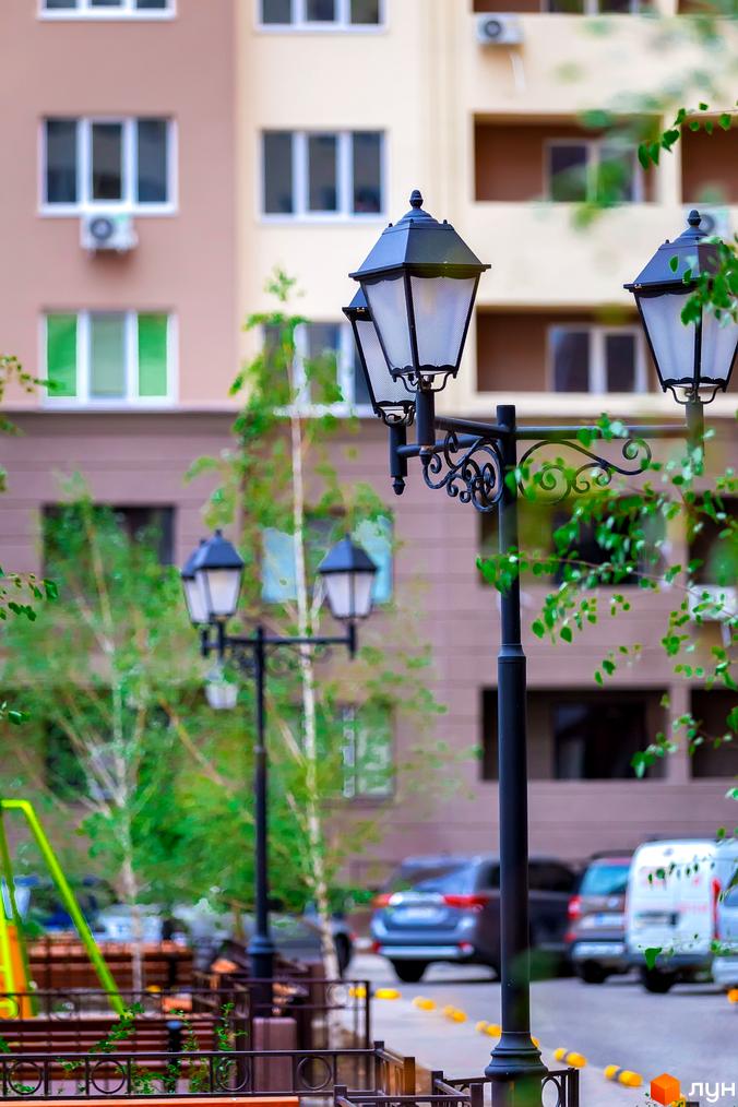 Житловий комплекс Одеські традиції: вид на фасад будинку та вуличні ліхтарі. На задньому плані припарковані автомобілі та зелені насадження.
