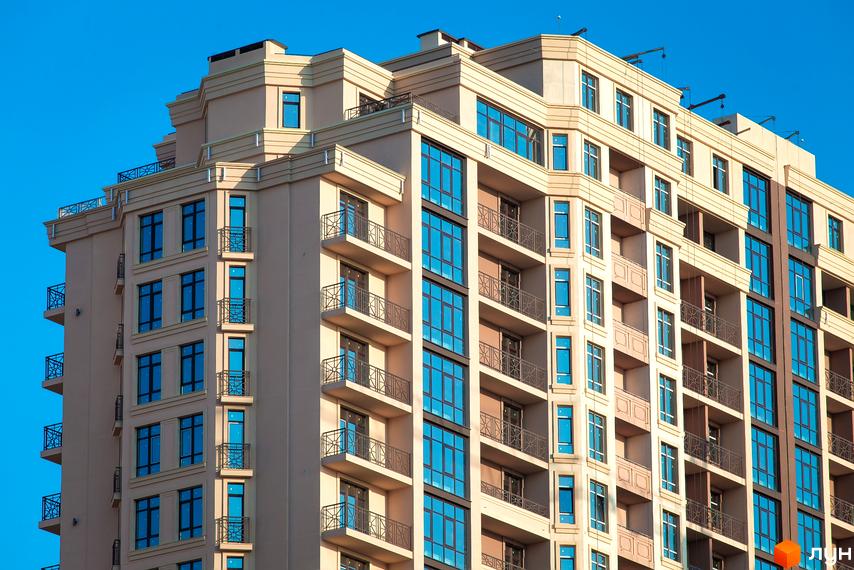 Елегія Парк - житловий комплекс з багатоповерховими будинками та балконами. Фасад будинку світло-бежевого кольору, вікна великі, блакитні.