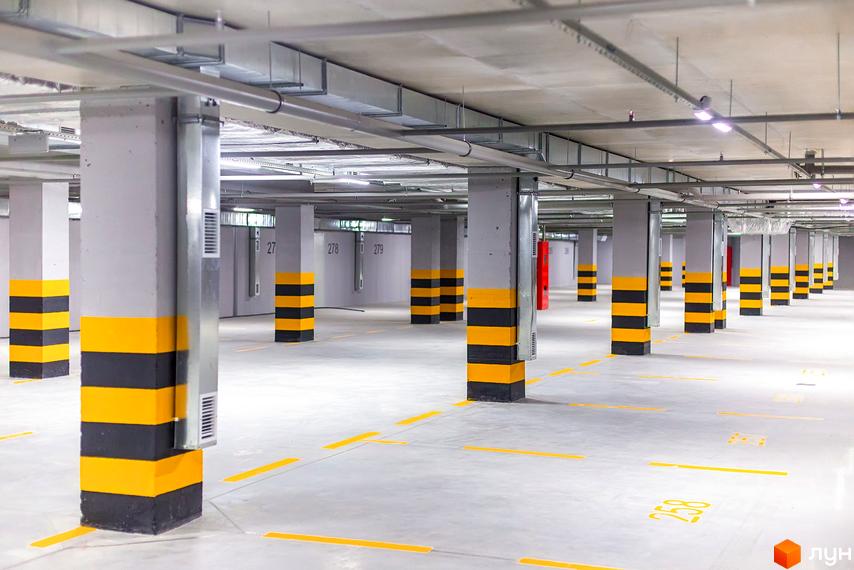 Підземний паркінг ЖК Елегія Парк з пронумерованими місцями та опорами з жовто-чорними смугами. Просторий паркінг з бетонною стелею та освітленням.