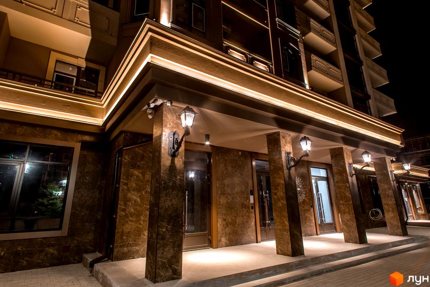 Житловий комплекс Елегія Парк. Фасад будинку з підсвіткою та ліхтарями біля входу. Територія біля будинку вимощена плиткою.