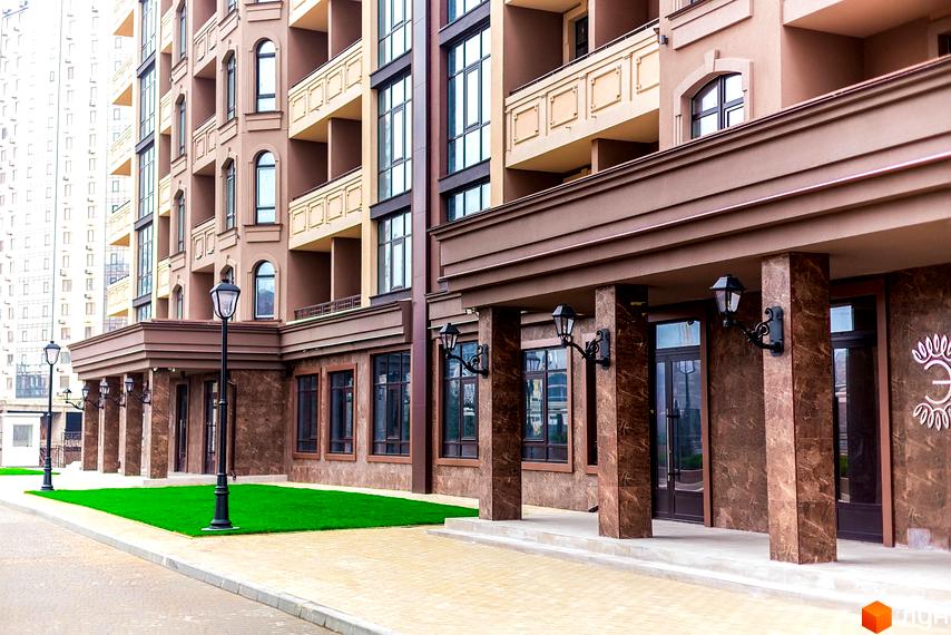 Фасад житлового комплексу Елегія Парк з мармуровими колонами та великими вікнами. Прибудинкова територія з акуратним газоном та бруківкою.
