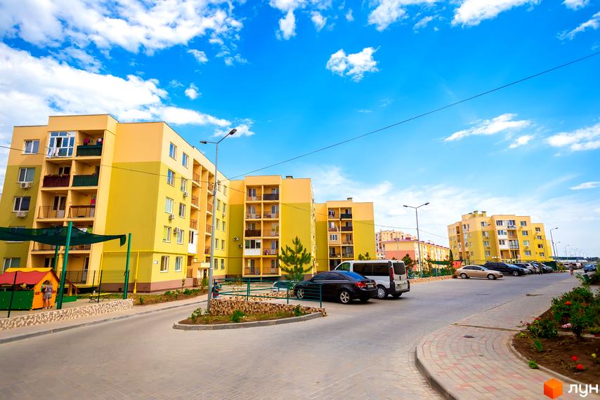 Житловий район Сьоме Небо з багатоповерховими будинками жовтого кольору та балконами. На території є дитячий майданчик, зелені насадження та парковка для автомобілів.