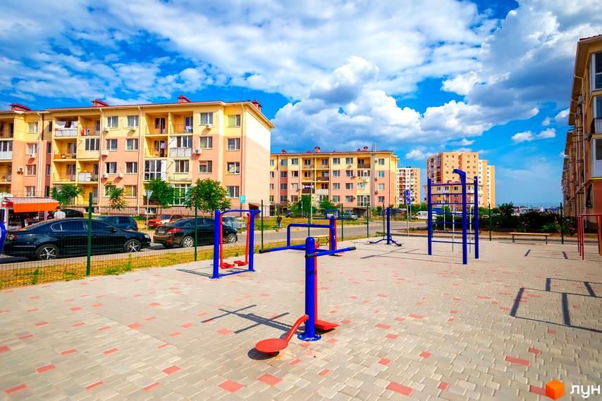 Житловий комплекс Сьоме Небо з фасадом у світлих тонах та прибудинковою територією з тренажерами на вулиці.