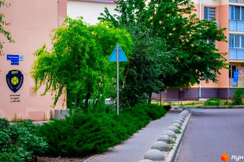 Зовнішній вигляд житлового комплексу ЖМ Сьоме Небо з зеленими насадженнями та пішохідною доріжкою.