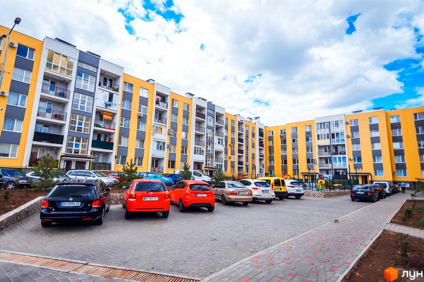 Житловий комплекс Сьоме Небо з жовтою фасадною частиною та прибудинковою територією, де паркуються автомобілі.