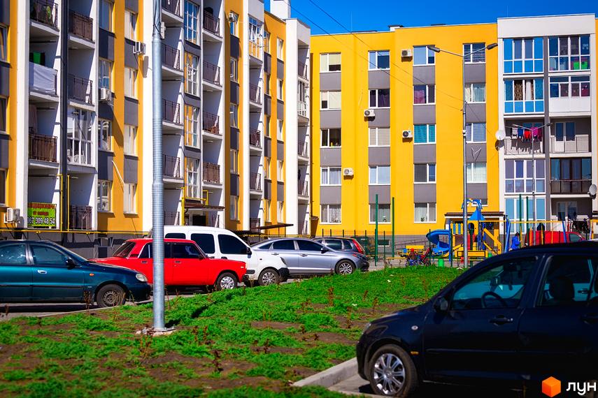 Житловий район Сьоме Небо: багатоповерхові будинки жовтого, сірого та білого кольорів з балконами. На прибудинковій території розташовані автомобілі та дитячий майданчик.