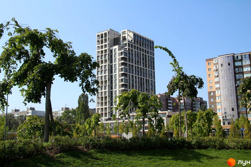 Висотна будівля ЖК Victory Hall з великою кількістю вікон. На передньому плані зелена трава та дерева.