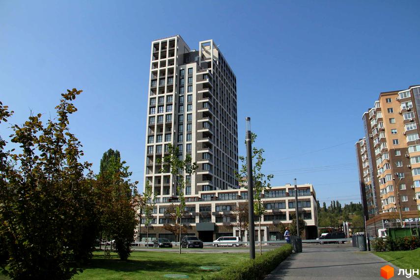 Висотна будівля ЖК Victory Hall з великою кількістю вікон та балконів. На передньому плані газон з деревами, тротуар та ліхтарі.