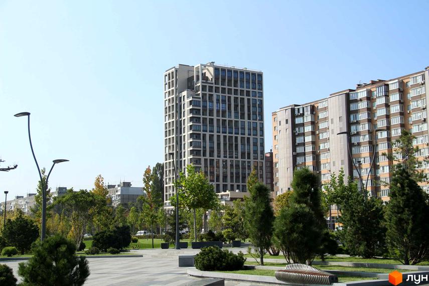 Висотна будівля ЖК Victory Hall з великою кількістю вікон. Поруч розташована доглянута прибудинкова територія з зеленими насадженнями та лавками.