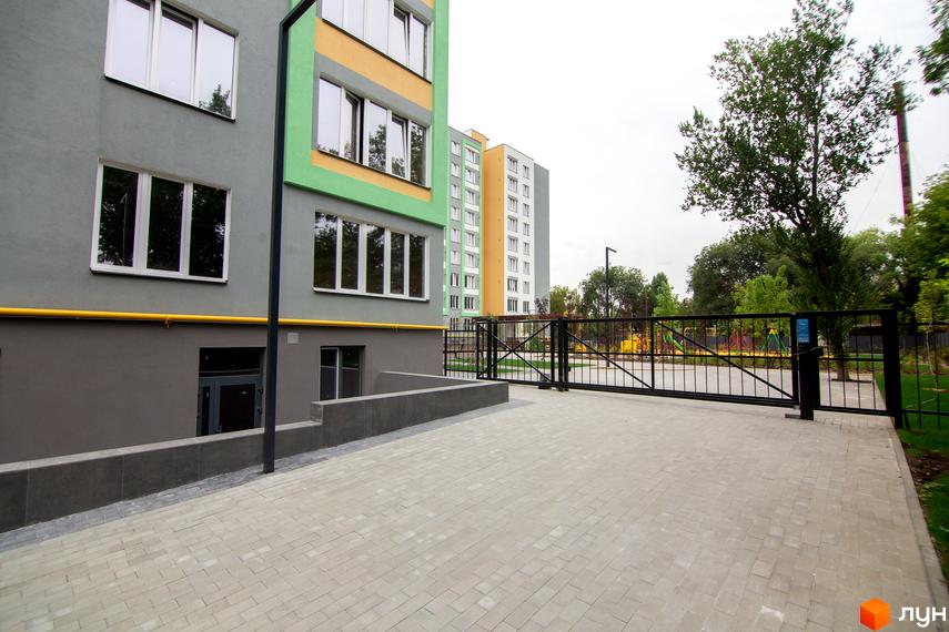 Житловий комплекс 3V Volkova. Фасад будинку сірого та зеленого кольору, огороджена територія з дитячим майданчиком.