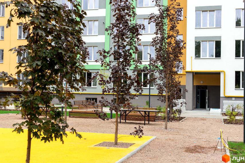 Житловий комплекс 3V Volkova. Фасад будинку з жовтими та зеленими вставками, прибудинкова територія з деревами та лавками.