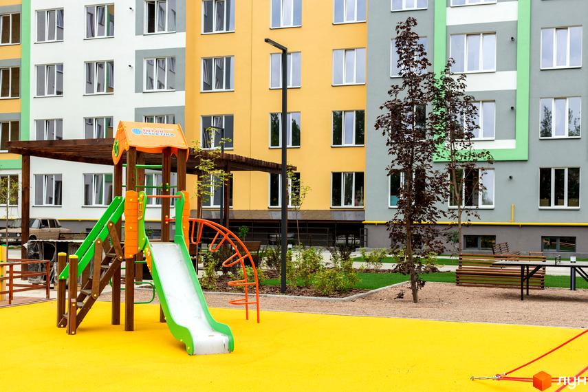 Житловий комплекс 3V Volkova з яскравим фасадом та дитячим майданчиком. На території комплексу розташовані лавочки та зелені насадження.