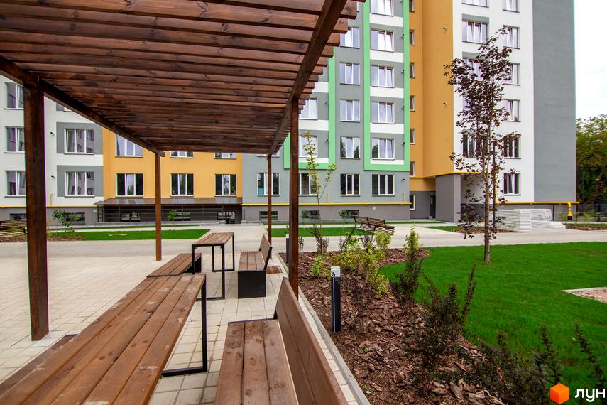 Житловий комплекс 3V Volkova: фасади будинків у жовтих та зелених кольорах, зона відпочинку з дерев'яними лавками та перголою.