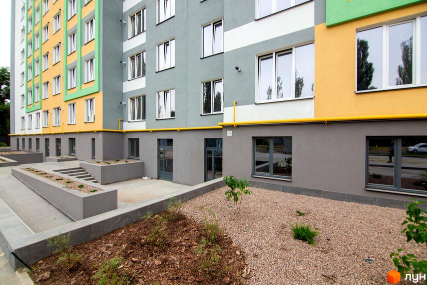 Новобудова 3V Volkova має багатоколірний фасад із численними вікнами. Прибудинкова територія включає бетонні доріжки та зони з гравієм.