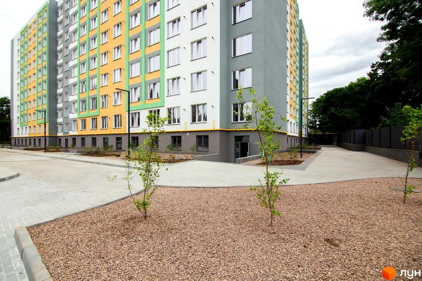 Житловий комплекс 3V Volkova. Зовнішній вигляд багатоповерхового будинку з жовтими та сірими фасадами, вікнами та прибудинковою територією з бруківкою та деревами.