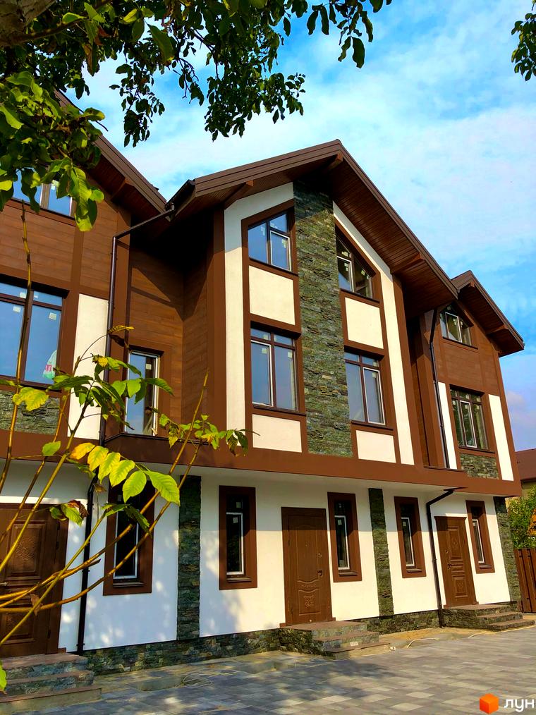 Зовнішній вигляд таунхаусів Київ Шале з оздобленням фасаду деревом, каменем та білою штукатуркою. Прибудинкова територія з тротуарною плиткою.