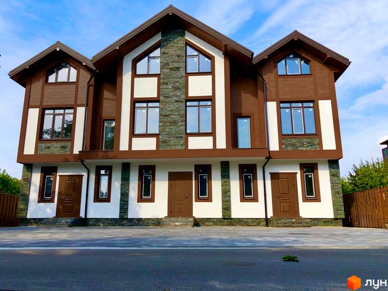 Зовнішній вигляд таунхаусів Київ Шале з коричневими та білими фасадами, кам'яними вставками та великими вікнами. Перед будинками облаштований двір з бруківкою та дорогою.