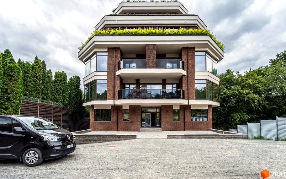 Будинок житлового комплексу на вул. Ломаківська (Мічуріна), 19б з цегляним фасадом та терасами з зеленню. Перед будинком розташований бруківковий двір та чорний мінівен.