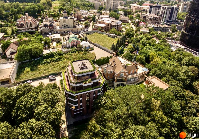 Вид на новобудову на вулиці Ломаківській, 19б, з багатою зеленою прибудинковою територією та іншими будівлями на фоні.