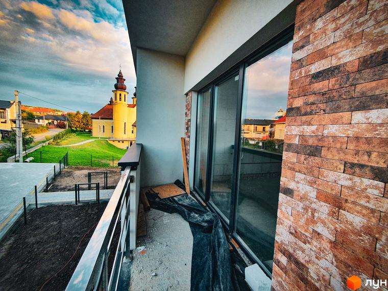 Житловий комплекс Клубний: вид з балкона на церкву та зелену територію. Зовнішній вигляд новобудови з цегляним фасадом та скляними дверима.