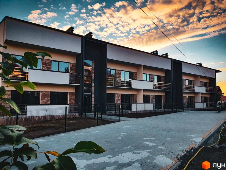 Зовнішній вигляд новобудови ЖК Клубний з балконами та вікнами, прибудинкова територія з бруківкою та огорожею.