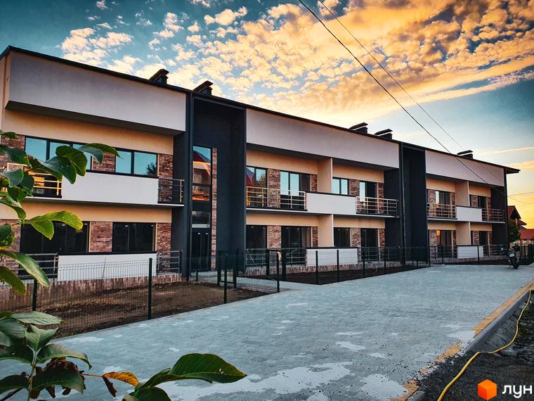 Зовнішній вигляд новобудови ЖК Клубний з балконами та цегляним фасадом. Прибудинкова територія з бруківкою та огорожею.